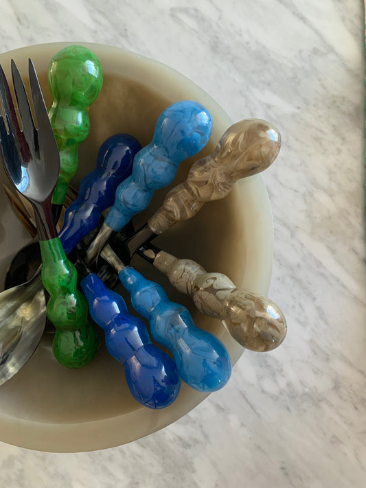 Two silver forks with green handles in a beige bowl on a marble surface
