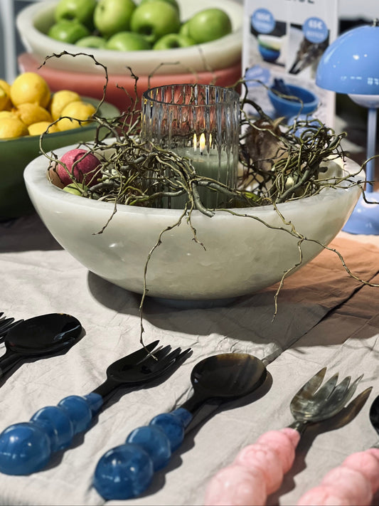 Table setting with white bowl, fruit, and cutlery on a light surface.