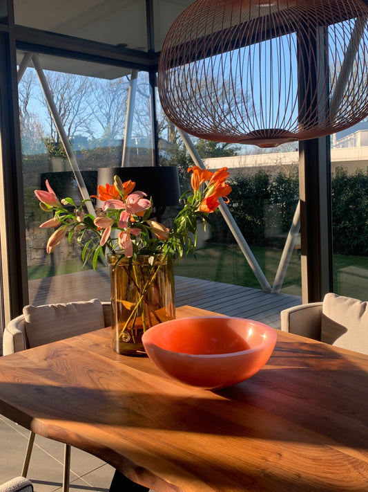 Wooden table with a vase of flowers and a pink Ohana bowl, hanging pendant light in the background.